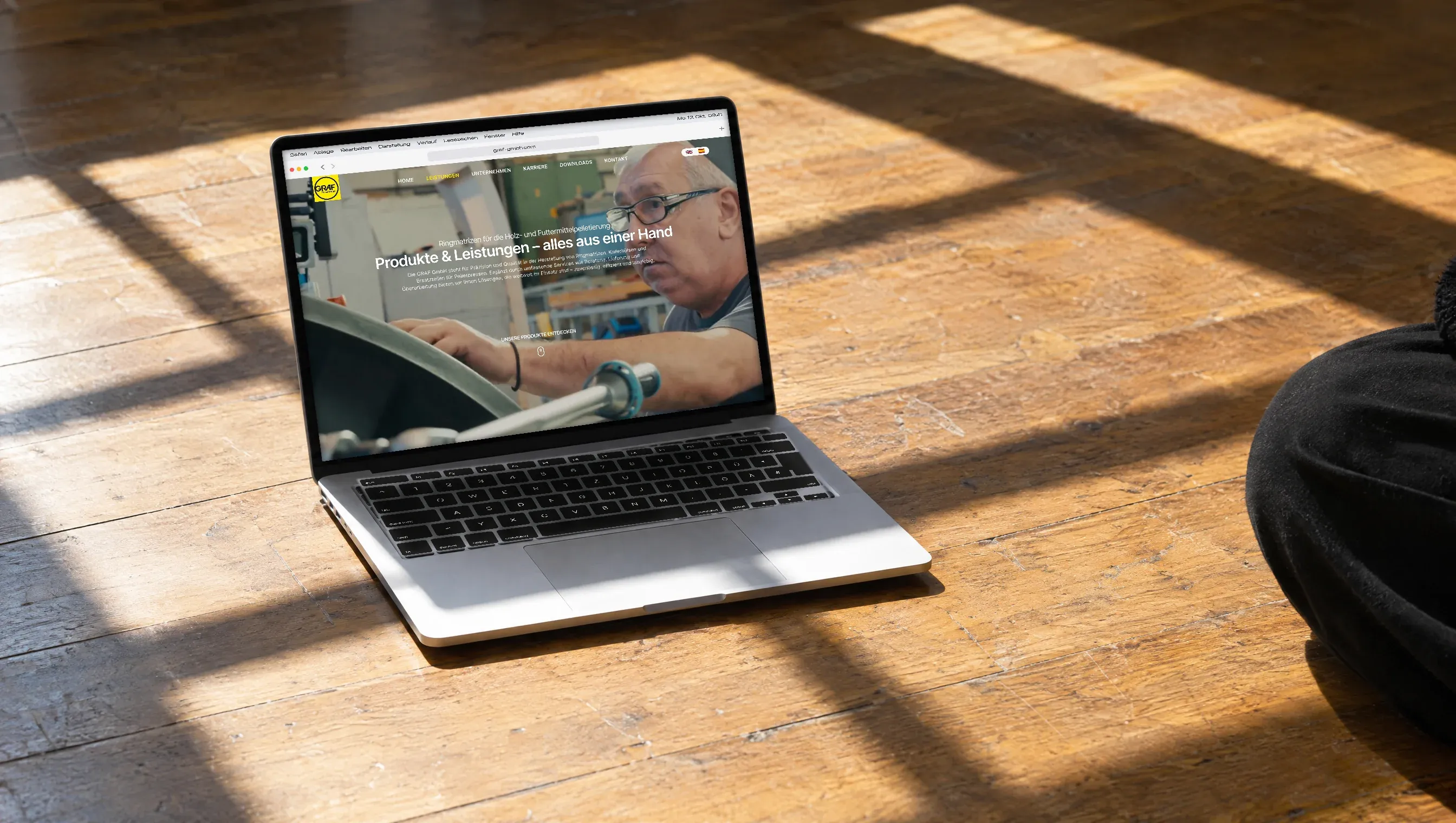 Ein Laptop mit der Seite Ringmatrizen der Graf GmbH steht auf alten Holzdielen im Sonnenlicht, das durch ein Fenster fällt