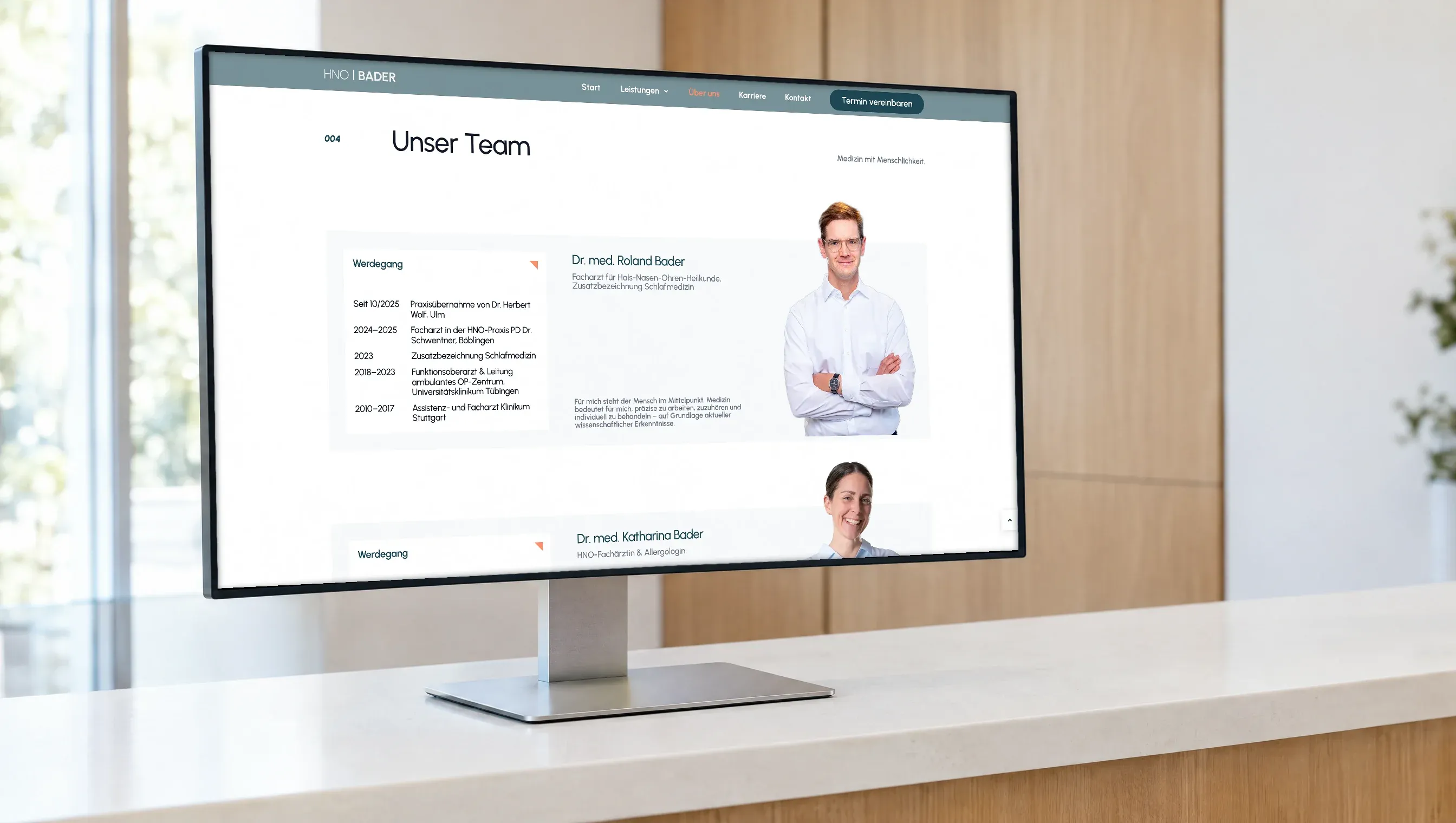 Ein Monitor auf dem Empfangstresen einer Praxis, darauf die Teamseite der HNO-Praxis Bader