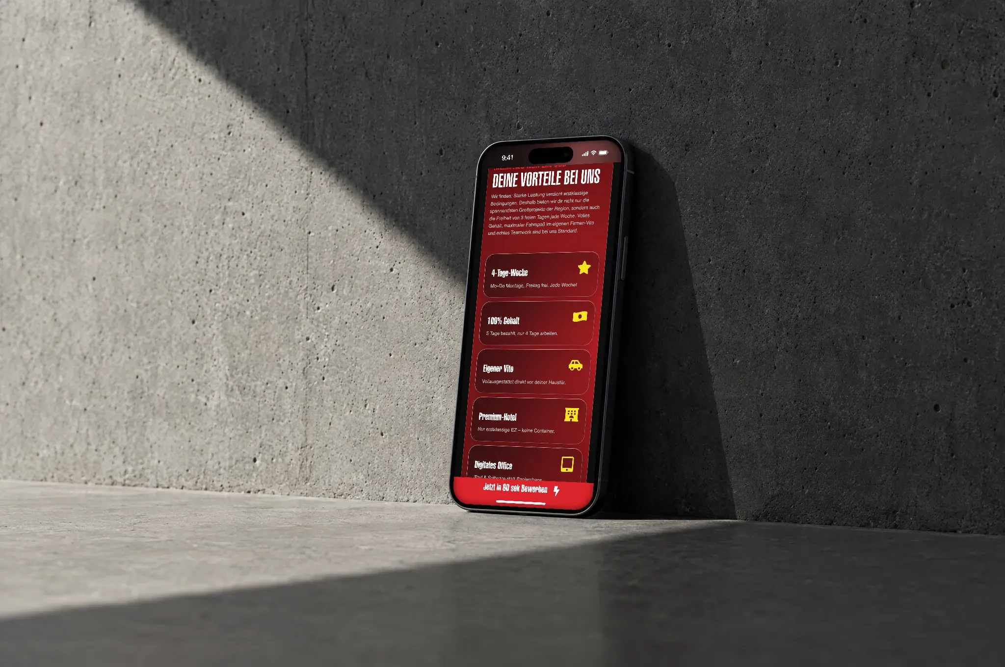 Ein Handy lehnt in der Sonne an einer Betonwand, darauf die Vorteile für Bauleiter der Deutschen Elektro in Rot mit gelben Symbolen