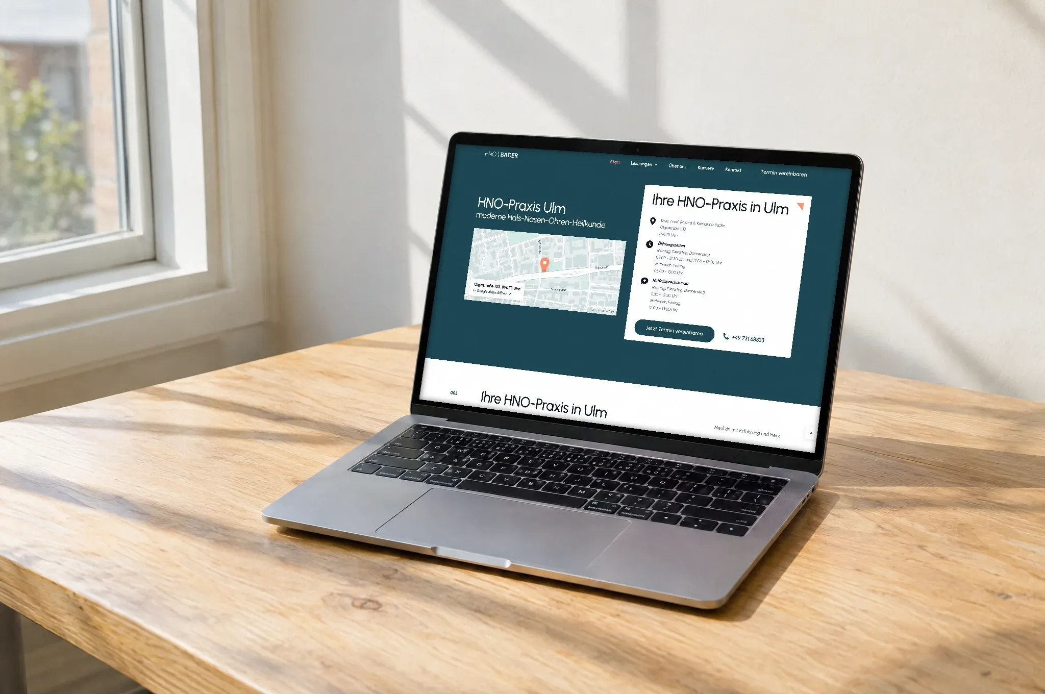 Ein Laptop auf einem Holztisch zeigt die Praxis-Website mit Karte und Öffnungszeiten in den Farben der Praxis