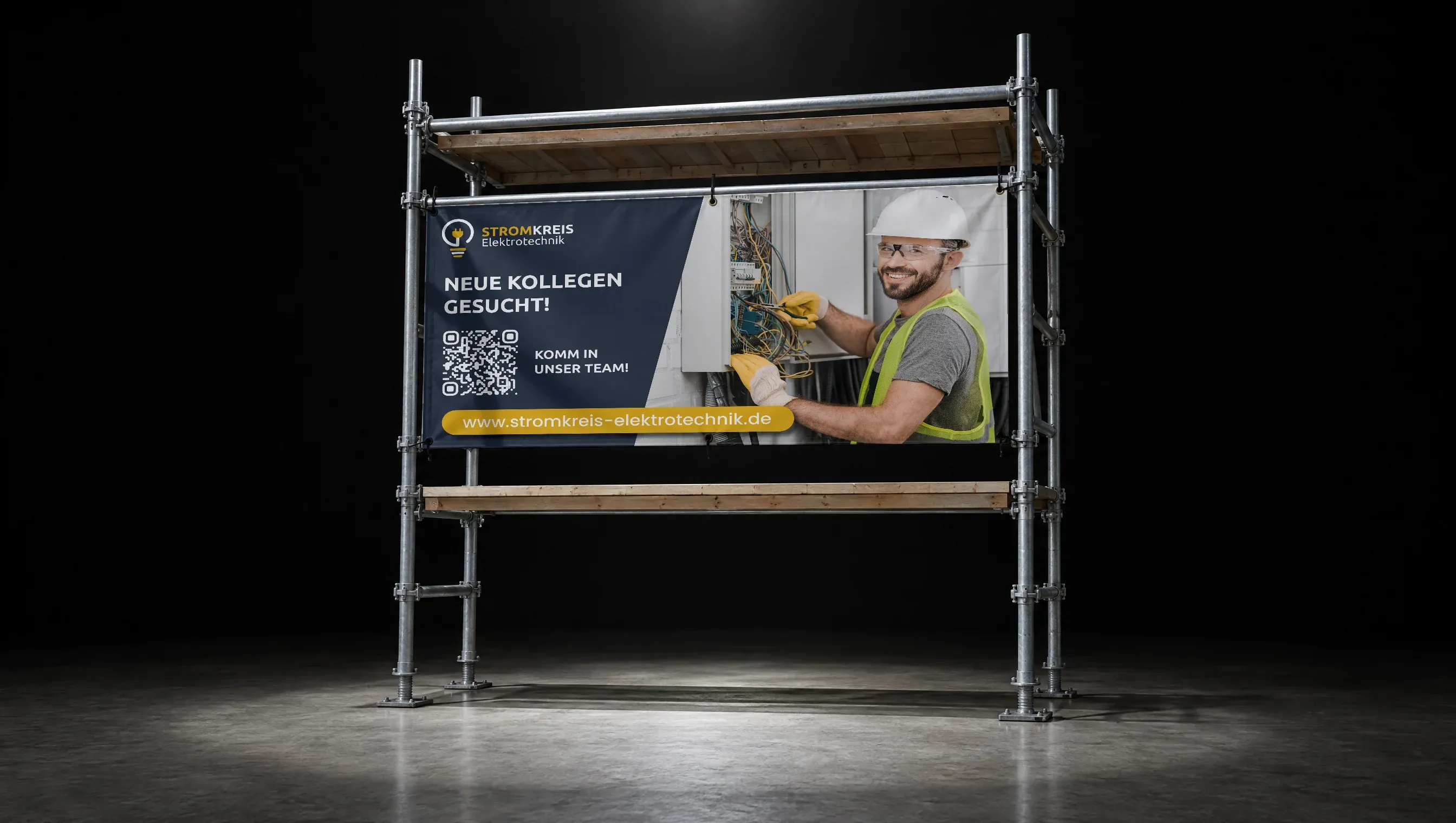 Das Banner „Neue Kollegen gesucht!" von Stromkreis Elektrotechnik hängt an einem Gerüstfeld im Lichtkegel eines dunklen Studios