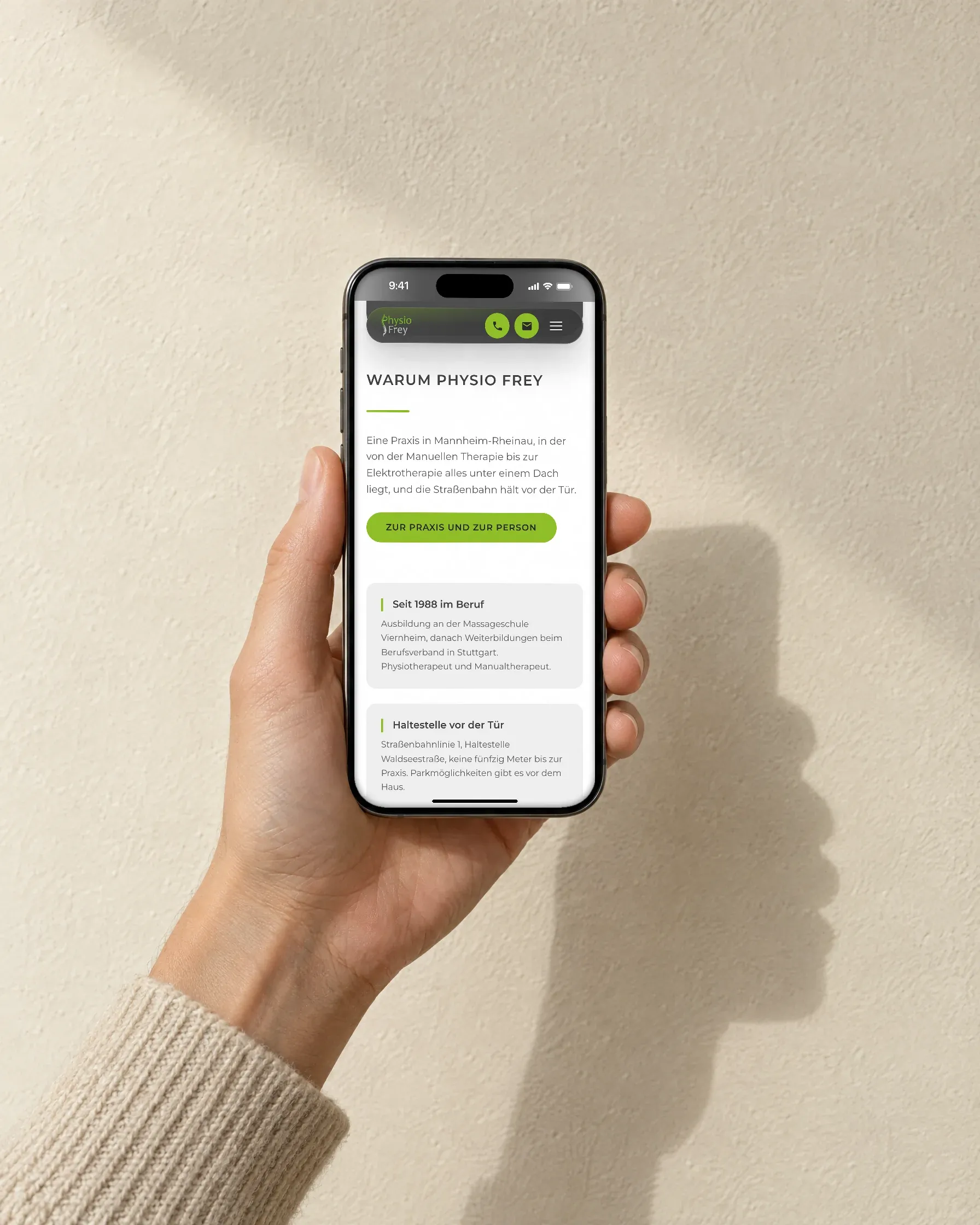 Eine Hand hält ein Handy vor einer hellen Kalkwand, auf dem Bildschirm der Abschnitt „Warum Physio Frey"