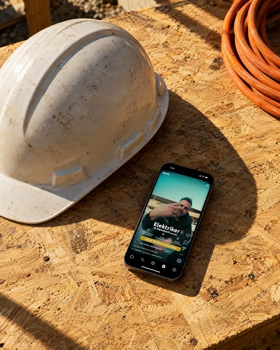Ein Handy neben einem weissen Bauhelm auf einer Holzplatte zeigt ein Reel von Stromkreis Elektrotechnik