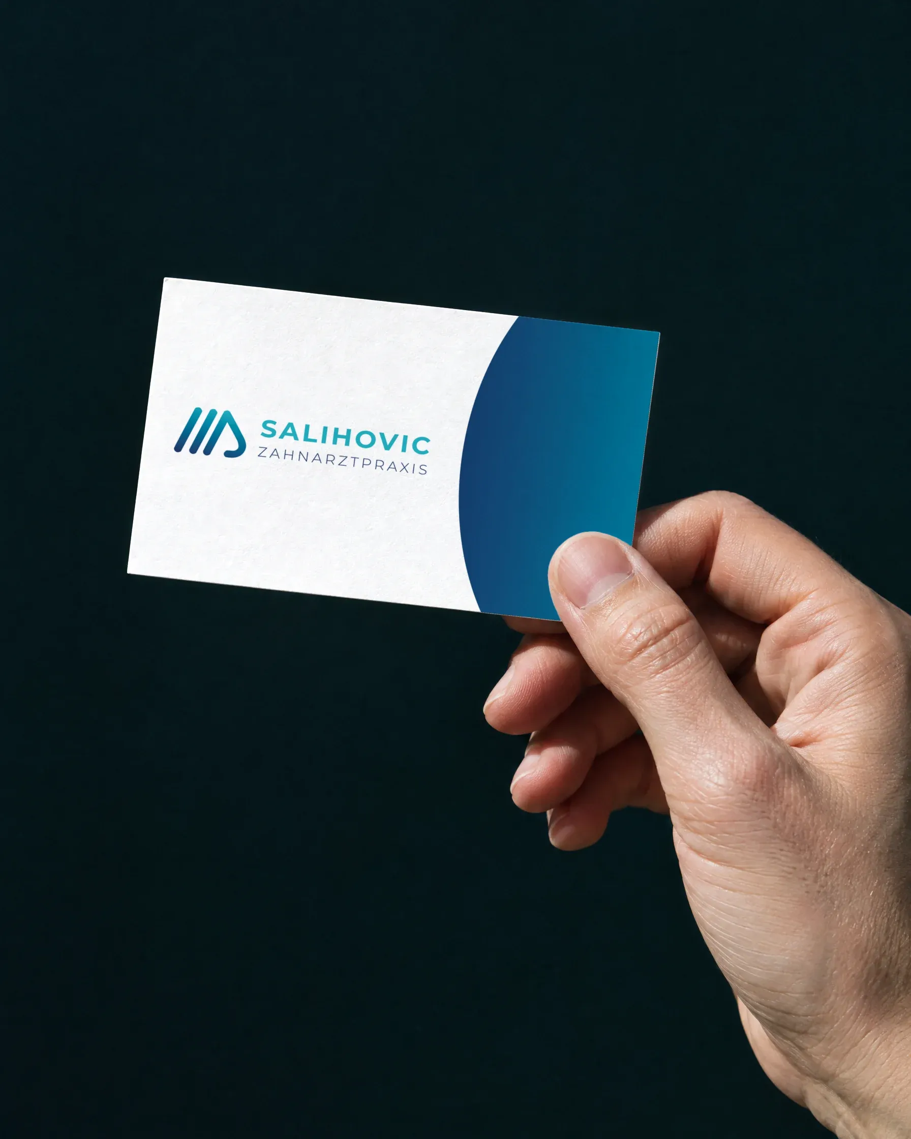 Eine Hand hält die Karte der Zahnarztpraxis Salihovic mit dem Logo vor dunklem Grund ins Sonnenlicht