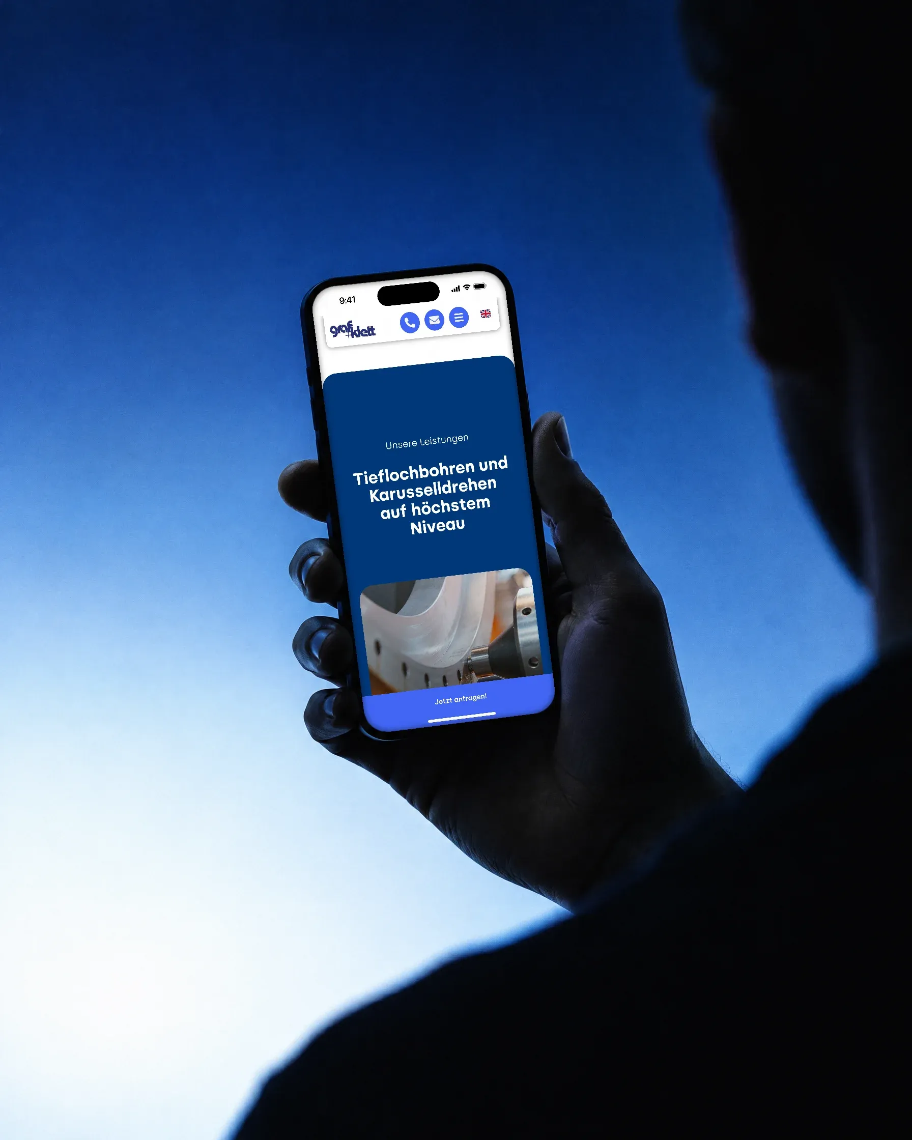 Über die Schulter gesehen: Eine Hand hält als Silhouette vor blauem Verlauf ein Handy mit den Leistungen von Graf + Klett
