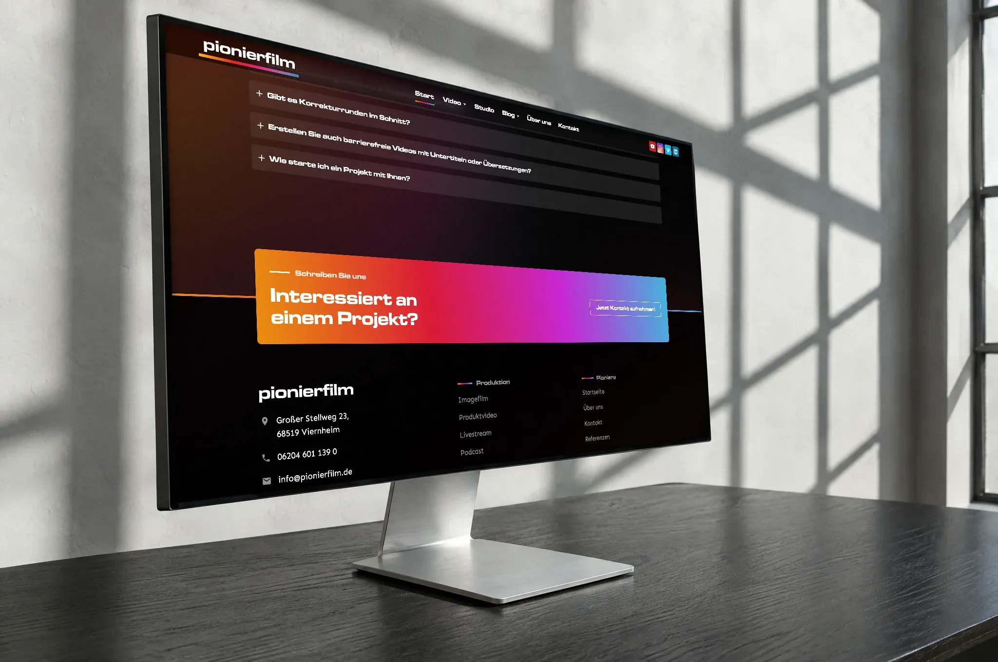 Ein Bildschirm von der Seite gesehen zeigt die Website von Pionierfilm mit einem Feld im Farbverlauf der Marke von Orange über Rot und Magenta nach Blau