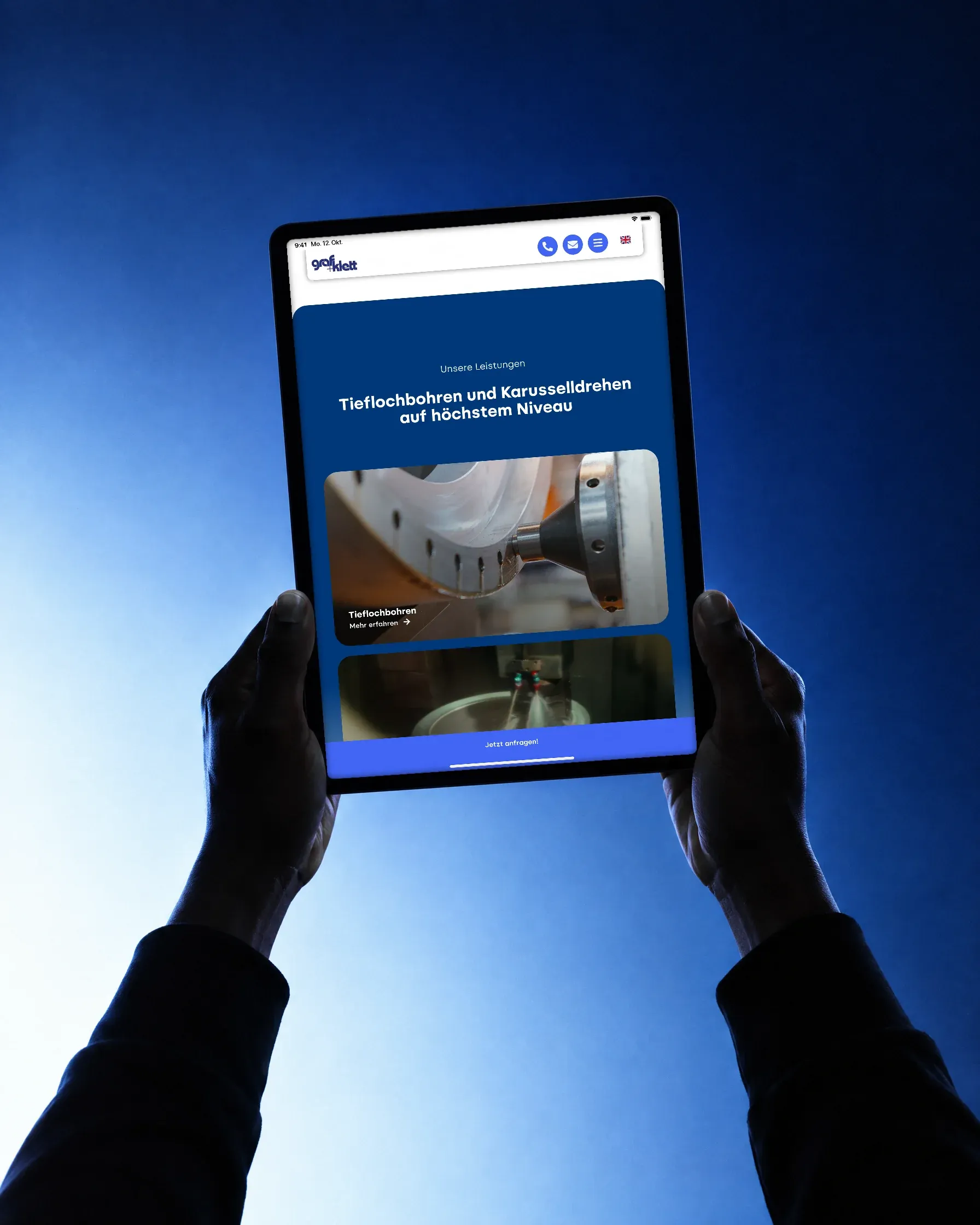 Zwei Hände halten vor blauem Verlauf ein Tablet hochkant, darauf Tieflochbohren und Karusselldrehen auf der Website von Graf + Klett