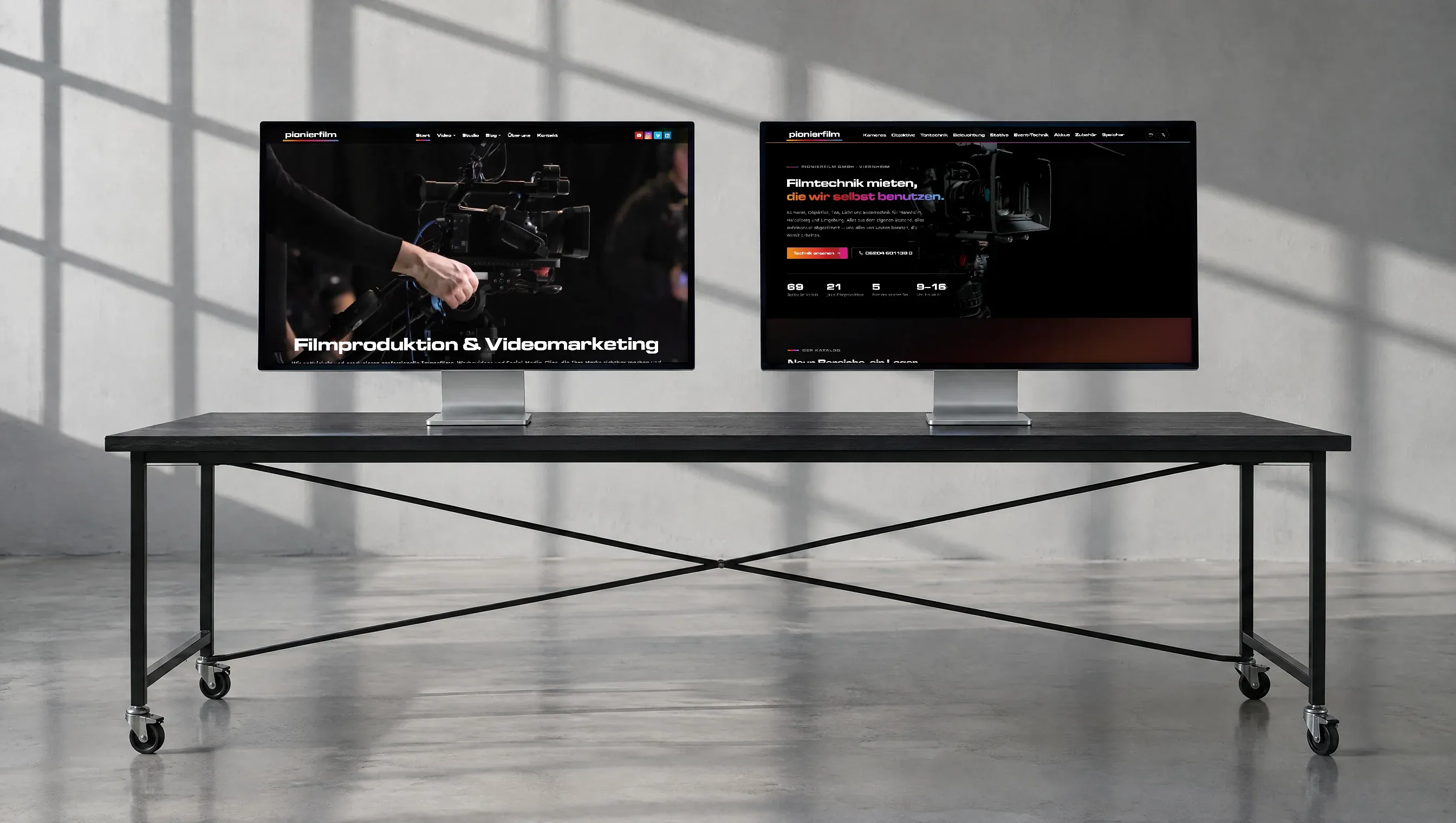 Zwei Bildschirme stehen nebeneinander auf einem langen schwarzen Tisch im Filmstudio, links die Website von Pionierfilm, rechts die des Kameraverleihs