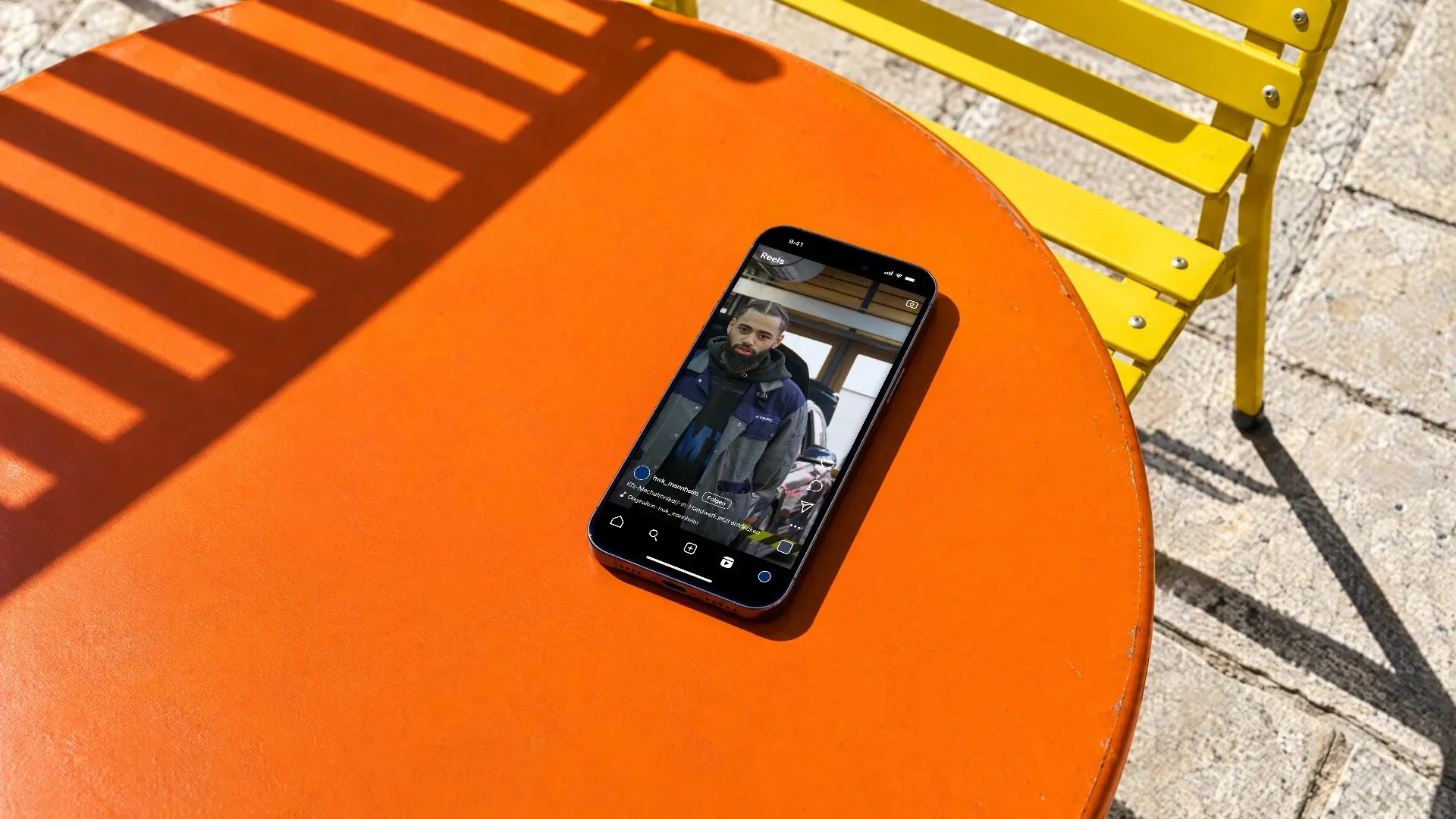 Ein Handy auf einem orangen Bistrotisch in der Sonne zeigt ein Reel der Handwerkskammer Mannheim