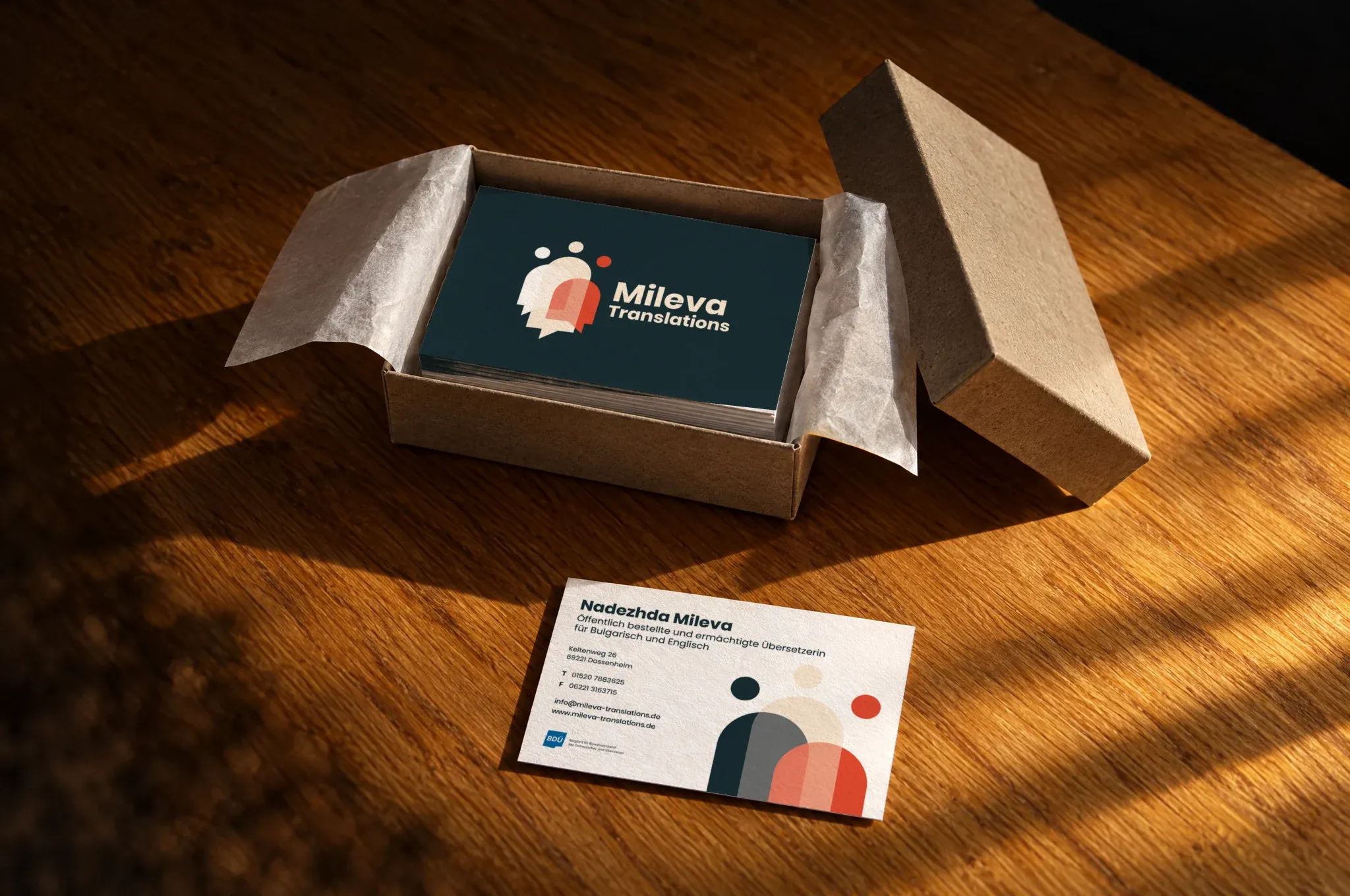 Ein geöffneter Karton mit einem Stapel Visitenkarten von Mileva Translations, halb aus dem Seidenpapier gepackt, davor eine Karte mit der Rückseite nach oben