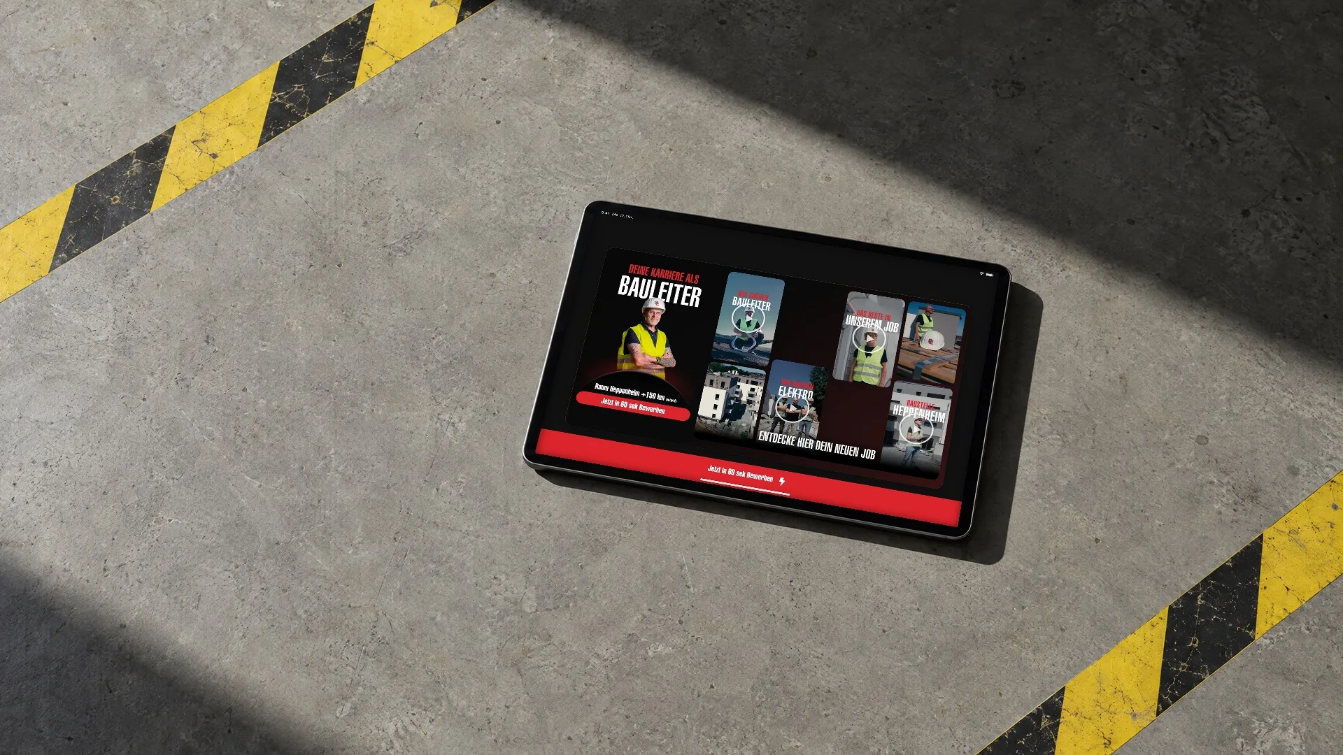 Ein Tablet liegt in harter Sonne auf Betonboden zwischen gelb-schwarzen Warnmarkierungen, darauf läuft die Karriereseite für Bauleiter der Deutschen Elektro durch