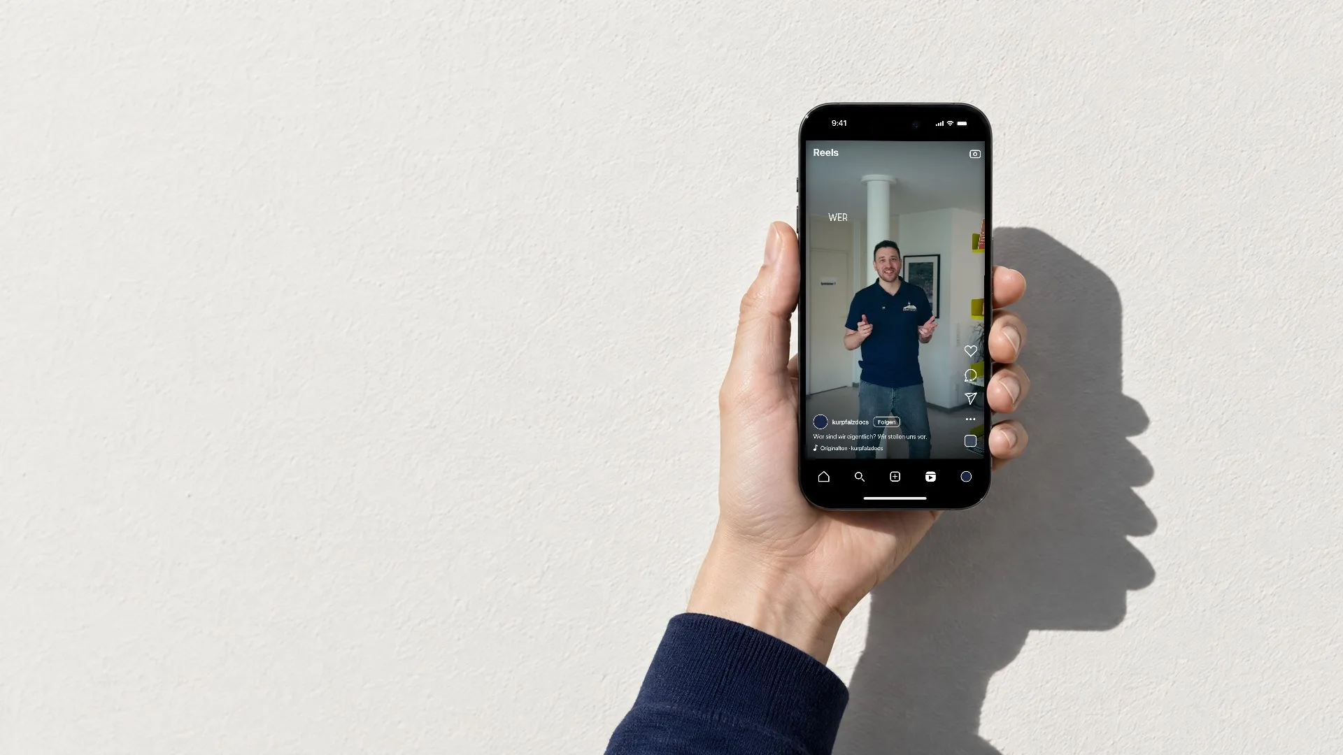 Eine Hand hält ein Handy vor eine weisse Wand in der Sonne, darauf stellen sich die Ärzte von Kurpfalz Docs in einem Reel vor